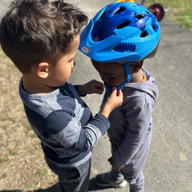 two children, one helping the other put on a bike helmet